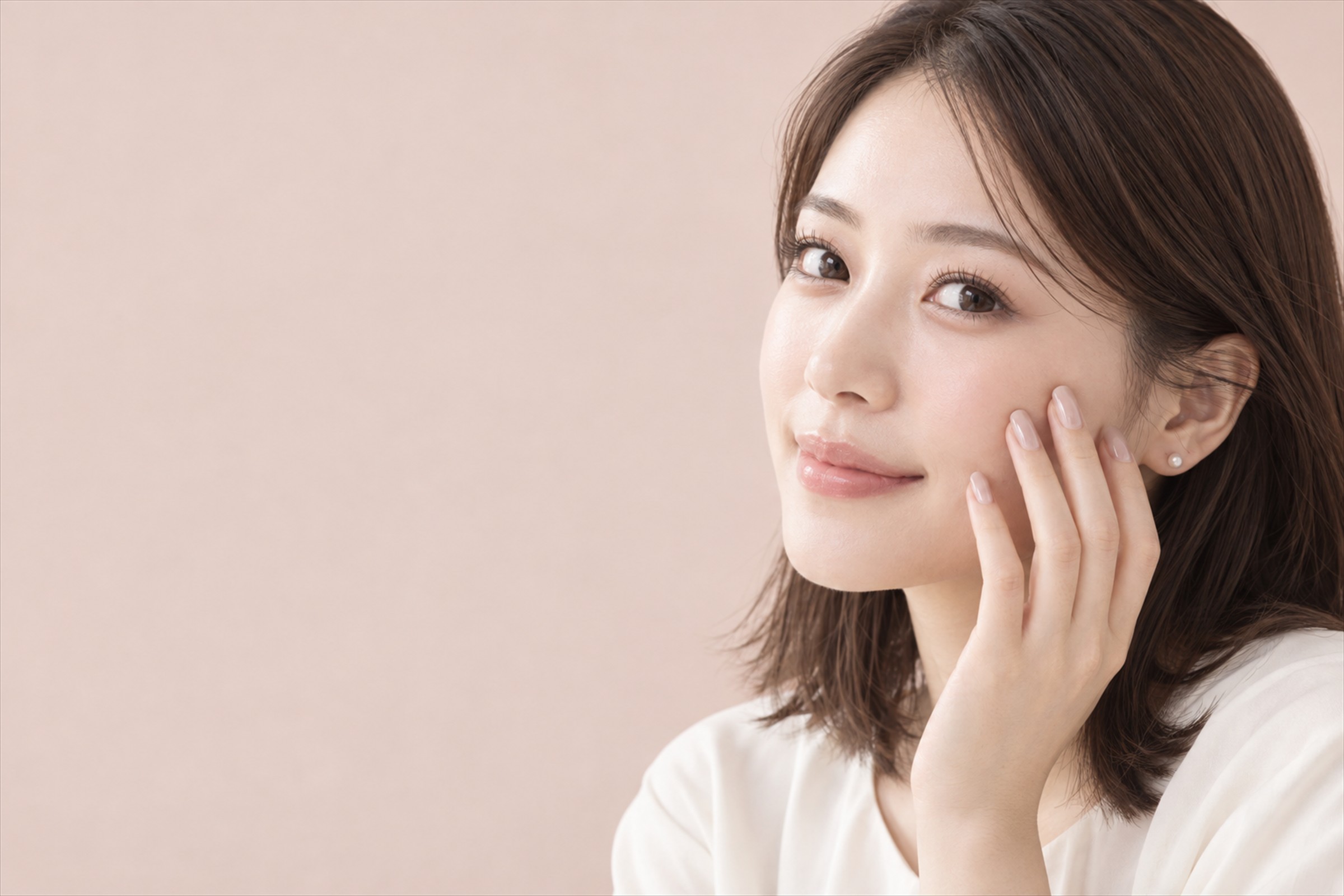 ミルクベージュのネイルの指先を頬に添えた、まつげパーマの女性